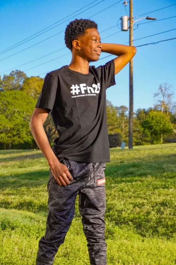 A young man standing in the grass holding his hand up to his head.