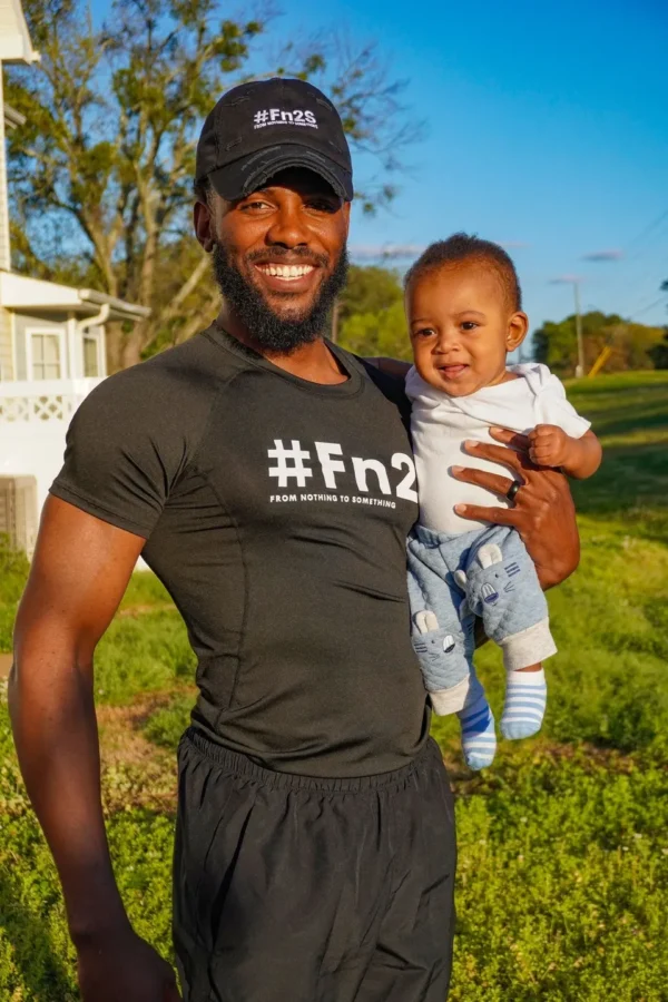 A man holding his baby in the grass.