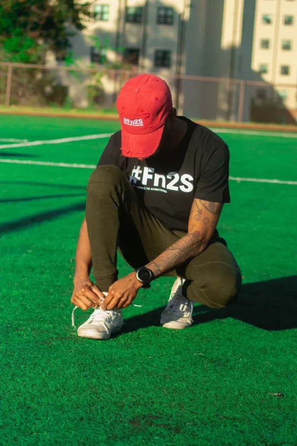 A man in black shirt tying his shoe on the grass.