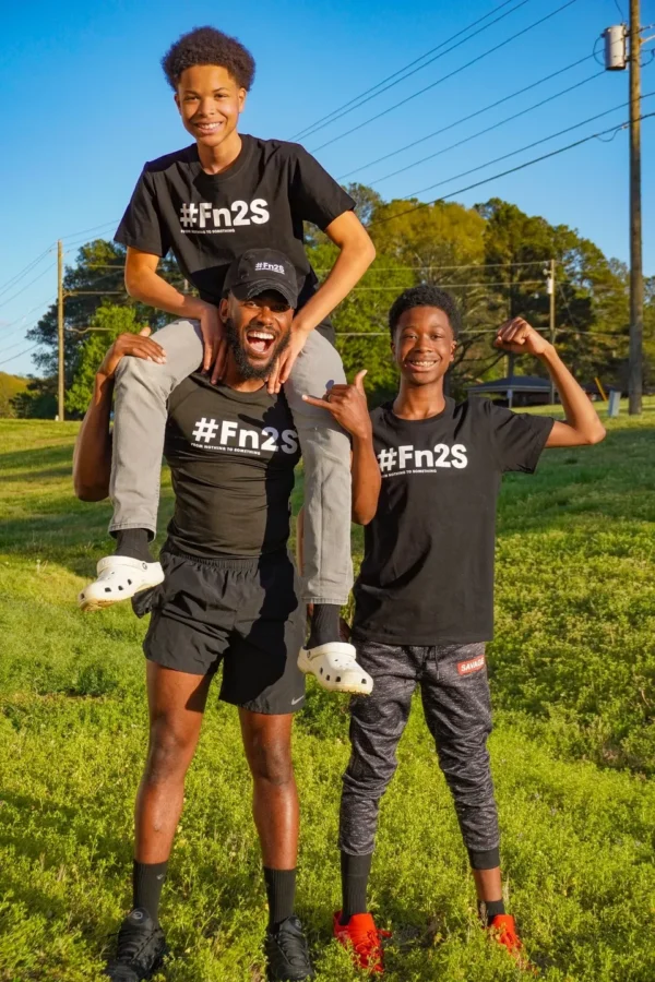 Three men in black shirts and shorts are posing for a picture.