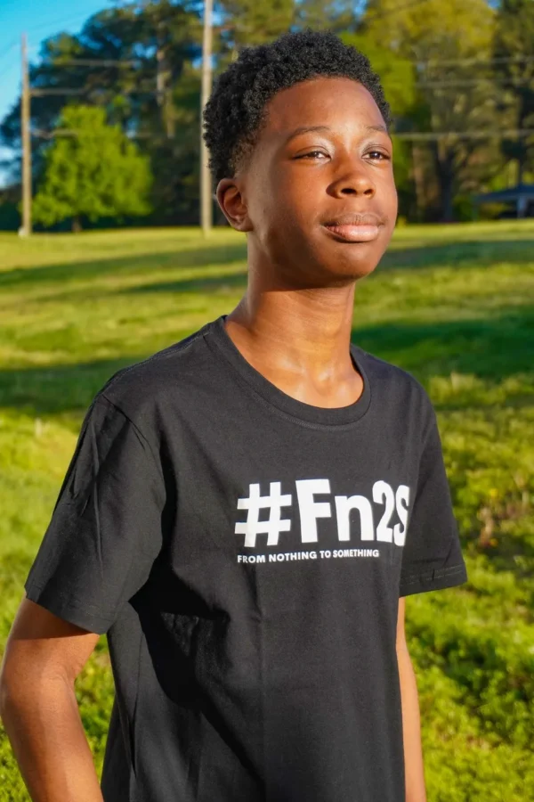 A young man wearing a black shirt standing in the grass.